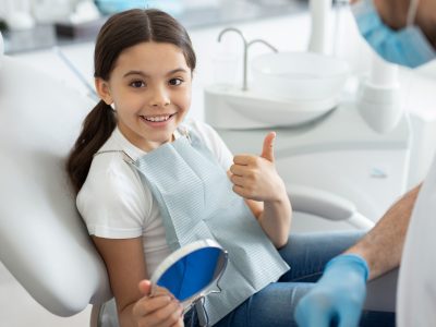 portrait of girl sitting in dental chair, showing thumb up and smiling at the camera portrait of girl sitting in dental chair, showing thumb up and smiling at the camera